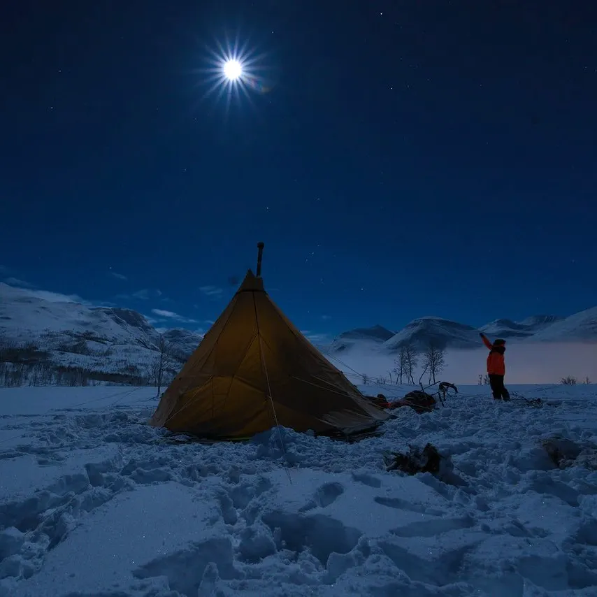 A tent in the snow under a bright moon