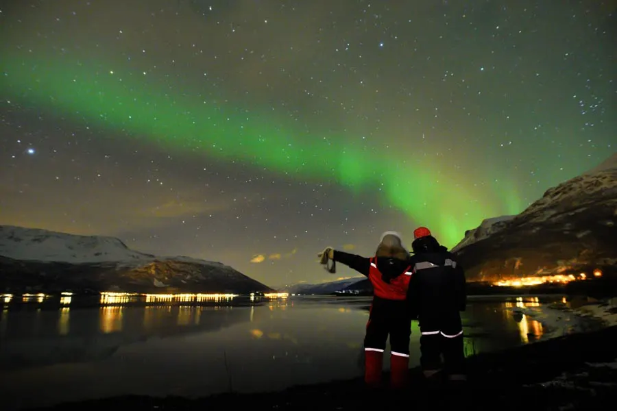 Two guests watching the aurora by the fjord