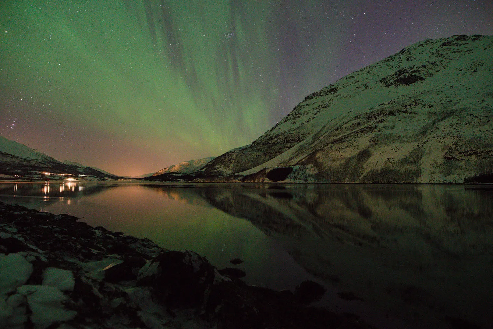 Aurora over a dark shoreline and village lights