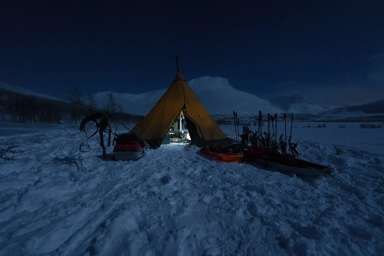 A lit tipi tent in the snow at blue hour