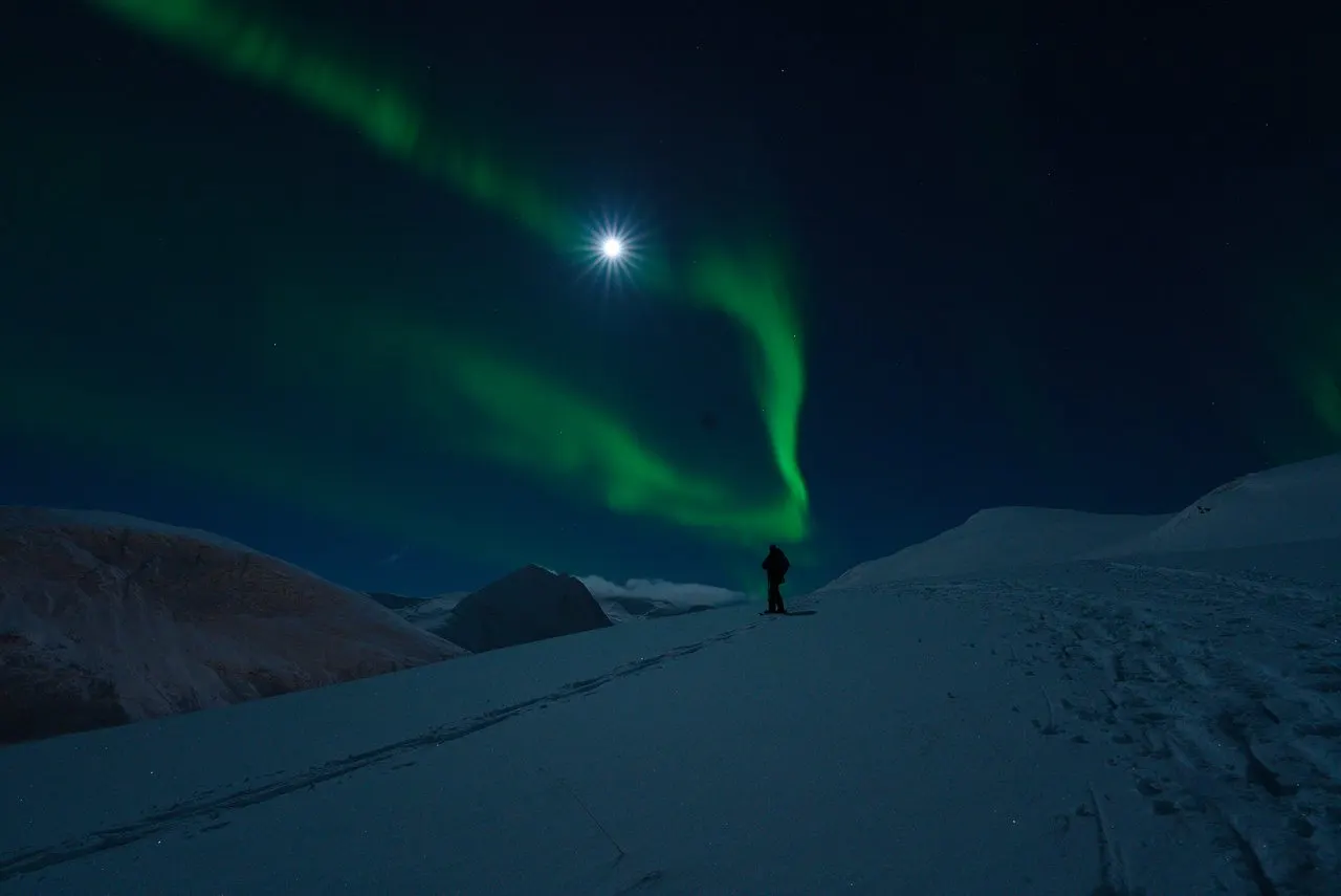 A lone figure under the aurora on a snowy plateau