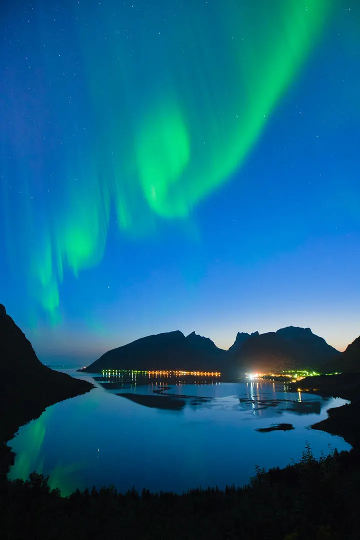 Aurora above a fjord and distant town lights