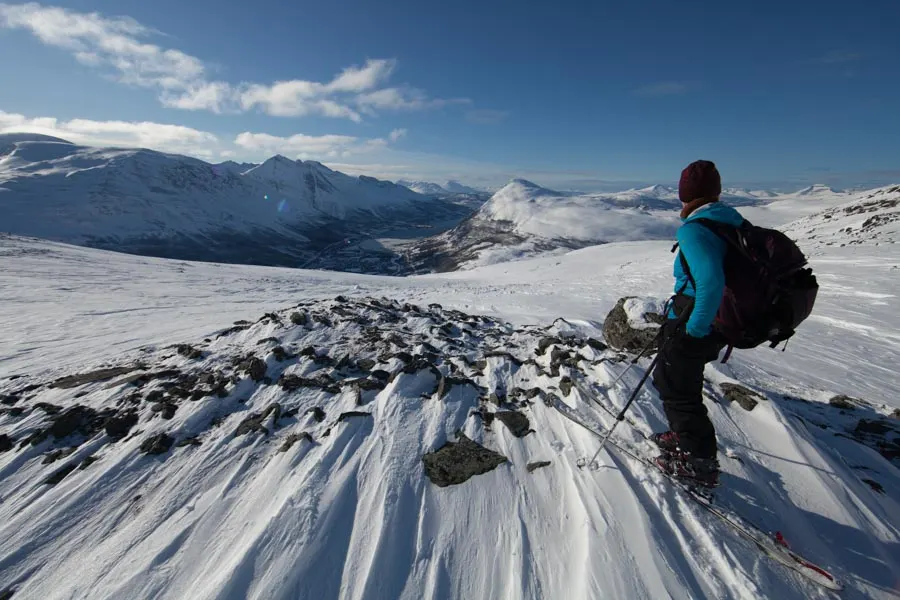 A hiker on a snowy summit looking over the mountains on a clear day