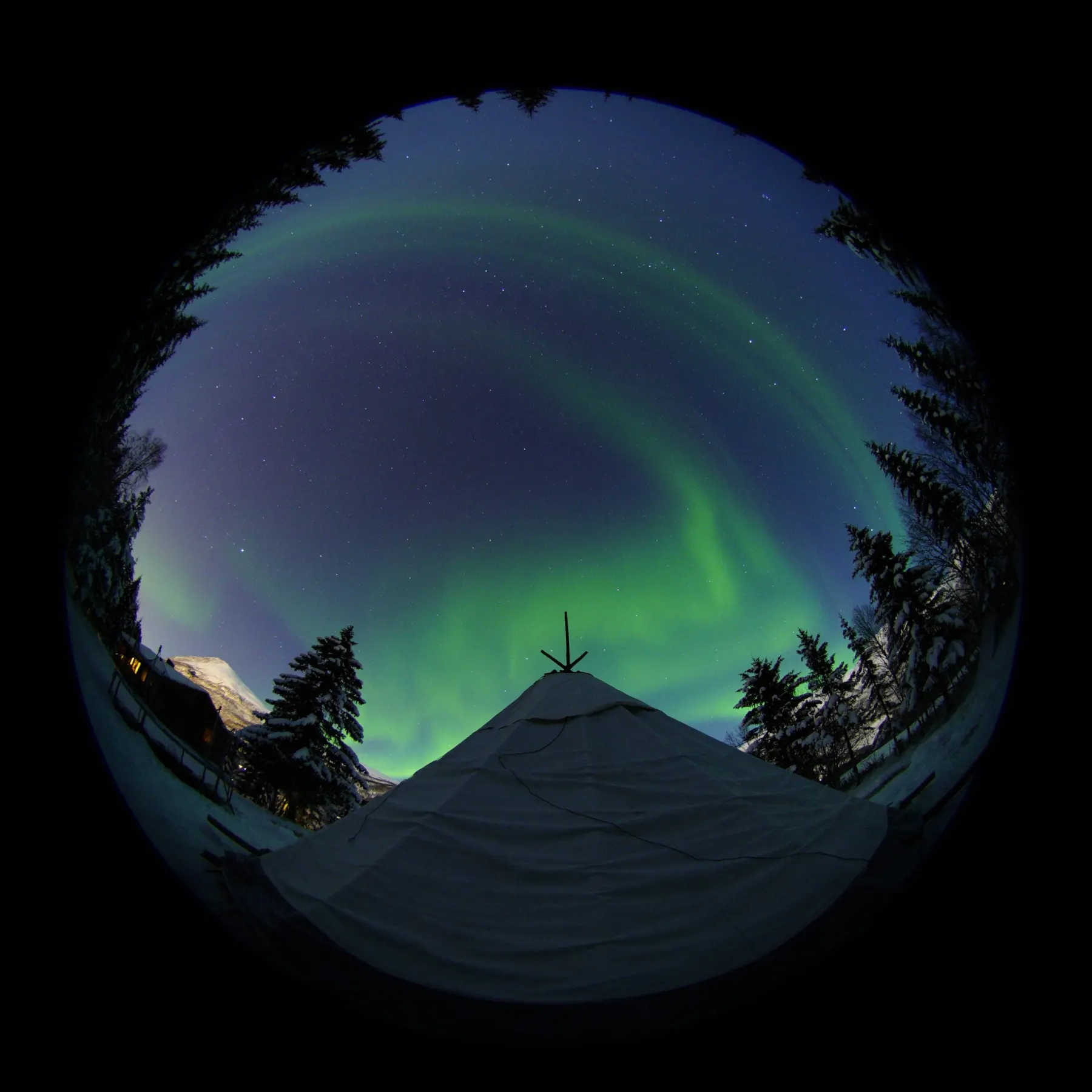 A tipi tent under a fisheye view of the night sky and aurora
