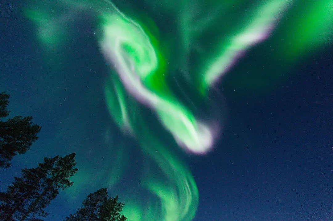 A spiral of green and pink aurora overhead